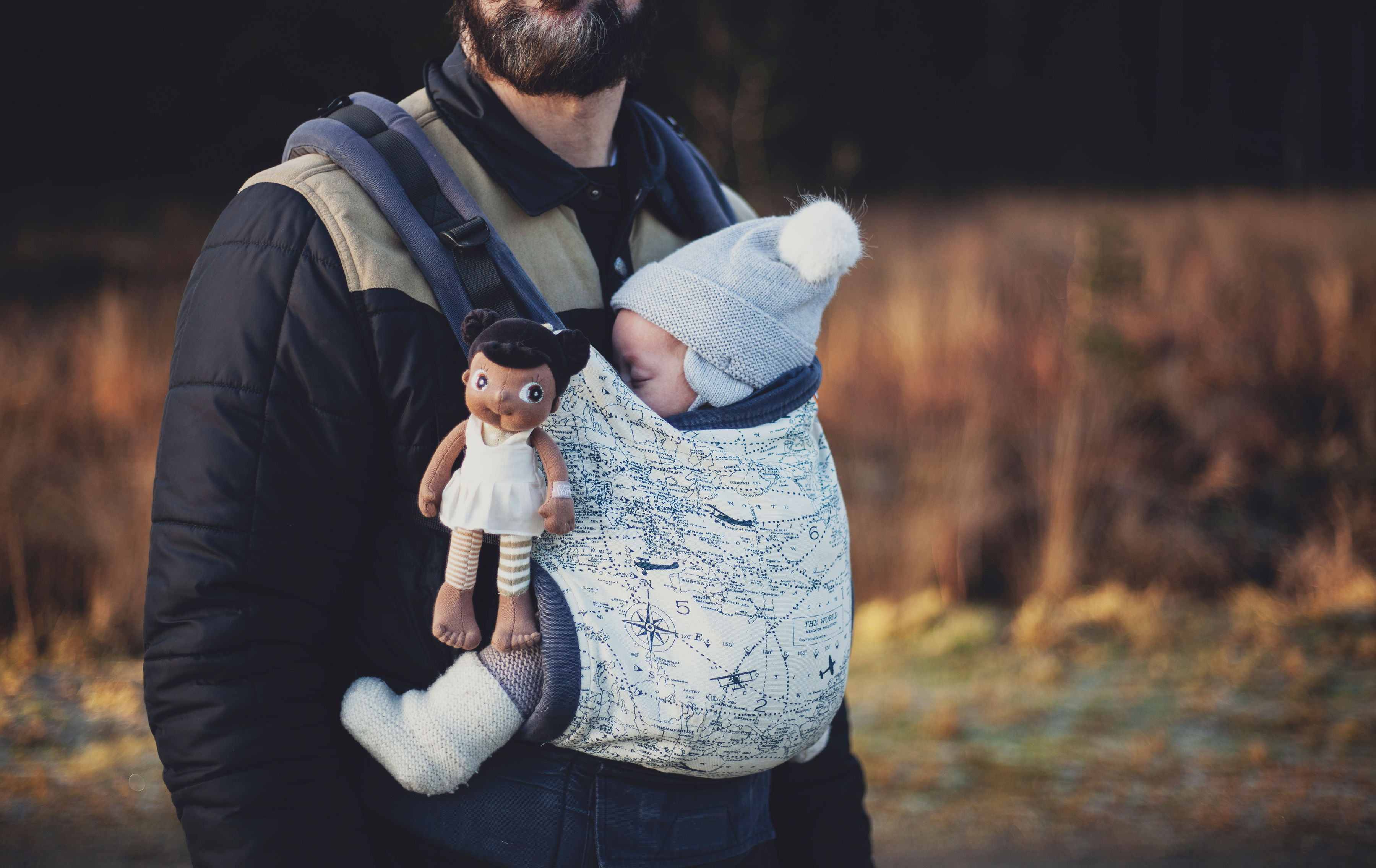 The Rubens EcoBuds mini doll Flora tucked into a baby carrier next to a baby