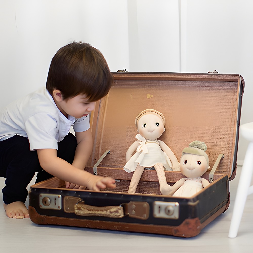 Child discovering two Rubens EcoBuds dolls in a vintage suitcase