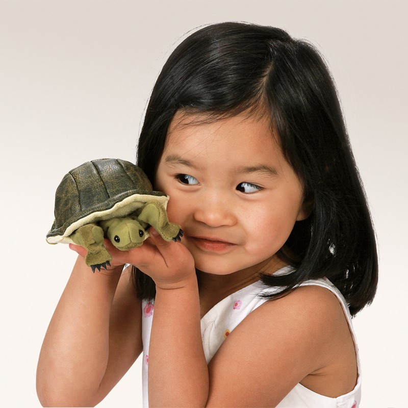 Young girl holding a Folkmanis mini turtle finger puppet with a dark green shell on her finger