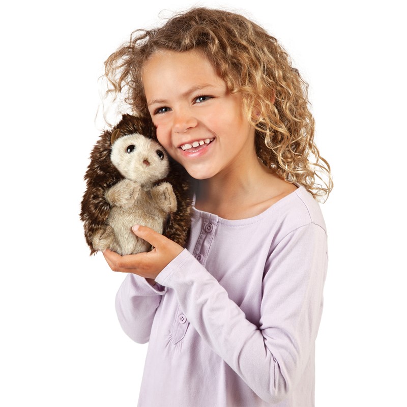 Smiling girl holding a Folkmanis hedgehog hand puppet with a brown spiny back and light belly fur in both hands