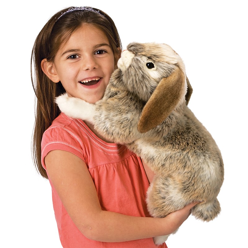 Mädchen hält die Folkmanis Handpuppe Widderkaninchen mit graubraun-meliertem Fell und herabhängenden Ohren in den Armen.