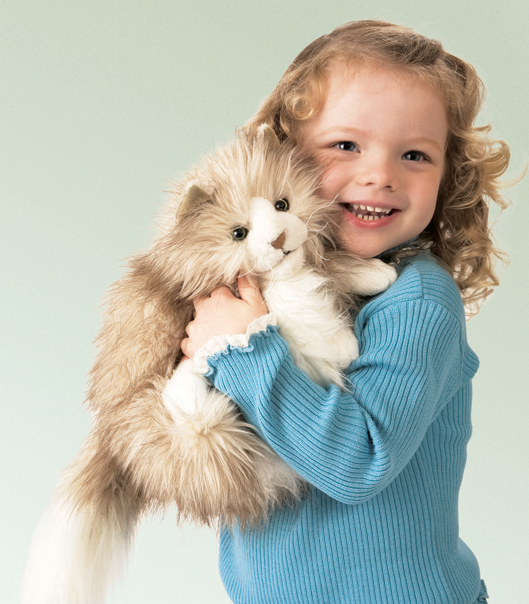 Lachendes Mädchen hält die Folkmanis Handpuppe flauschige Katze mit beigefarbenem Langfell und weißem Bauch im Arm.