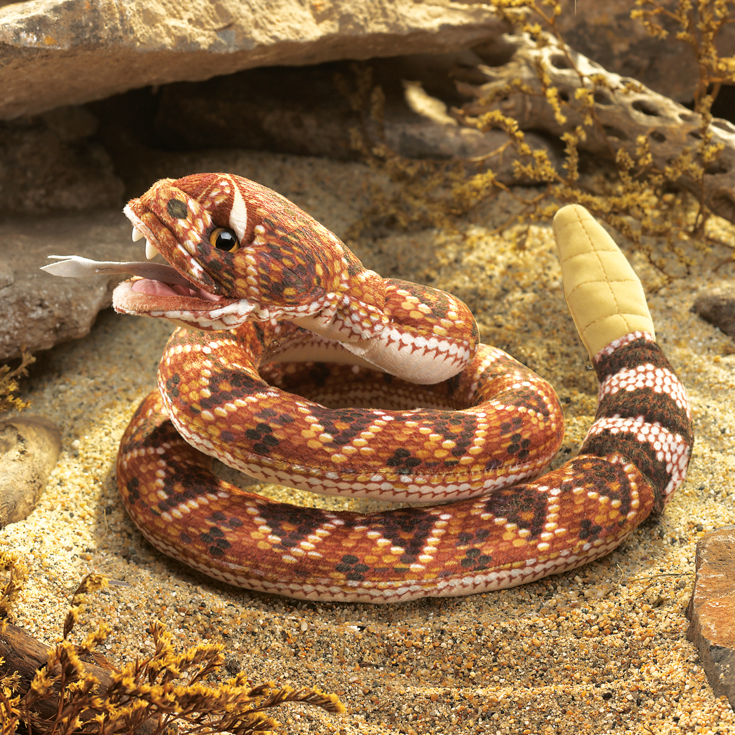 Folkmanis rattlesnake hand puppet with open mouth, forked tongue and yellow rattle tail, coiled on sand