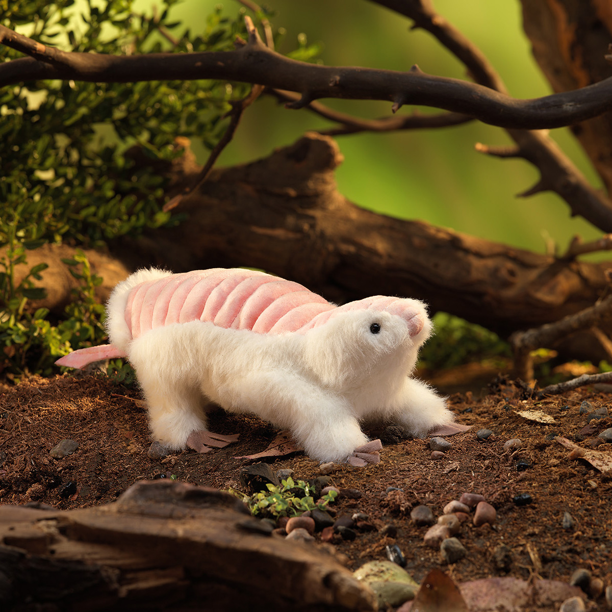 Folkmanis hand puppet pink fairy armadillo with white fur and pink shell, side view on a forest floor