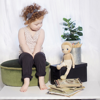 Child sitting next to a Rubens EcoBuds doll on a wooden box with pencil cup