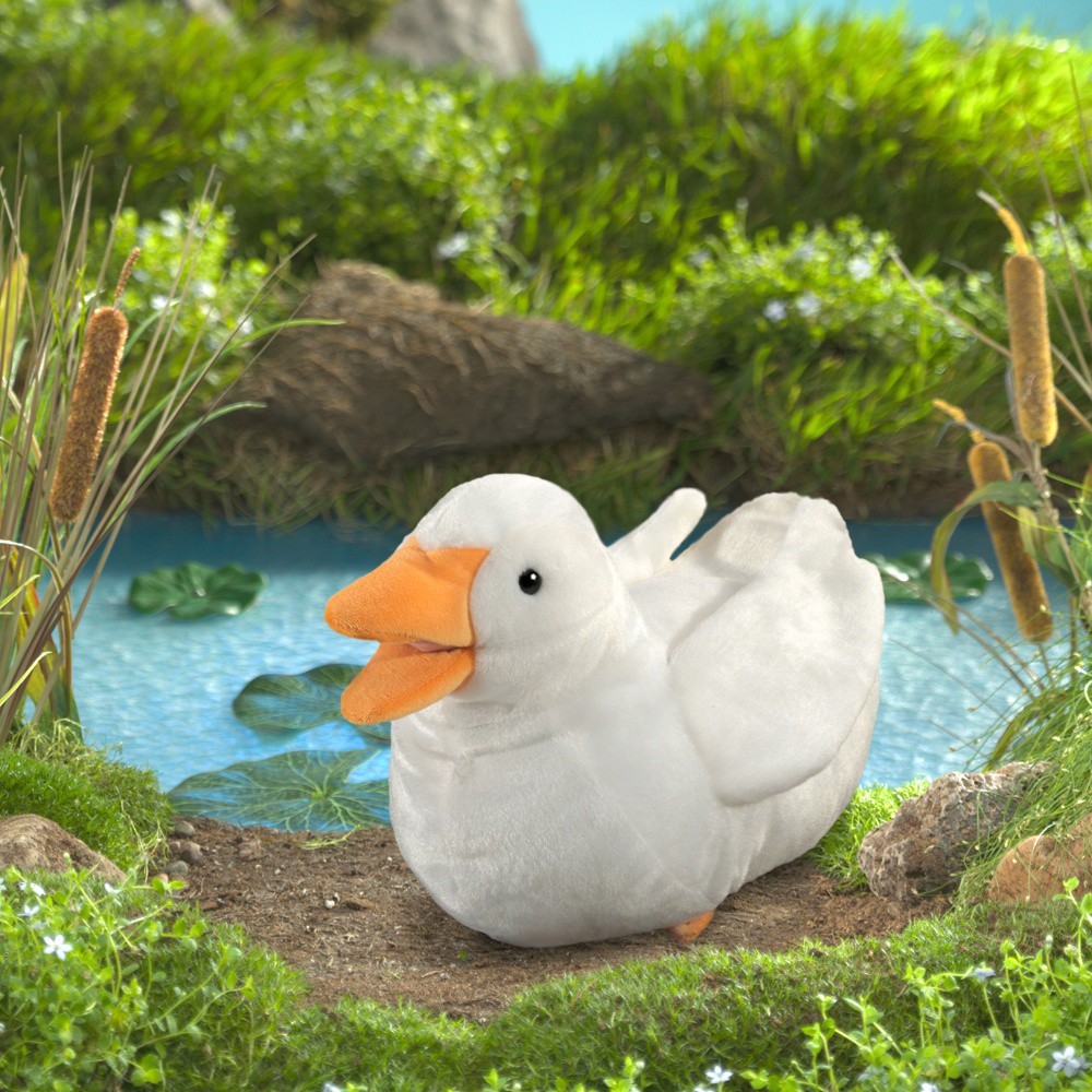 Folkmanis duck hand puppet in white with an orange beak, sitting in front of a pond with lily pads and reeds
