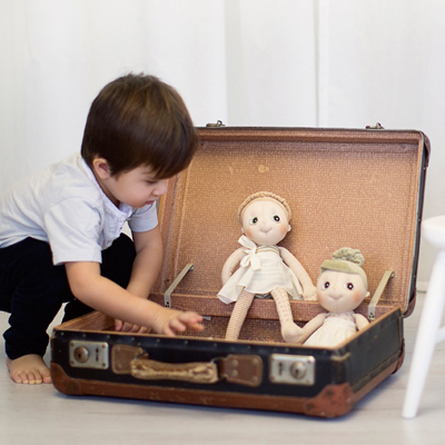Child playing with two Rubens EcoBuds dolls in an old suitcase