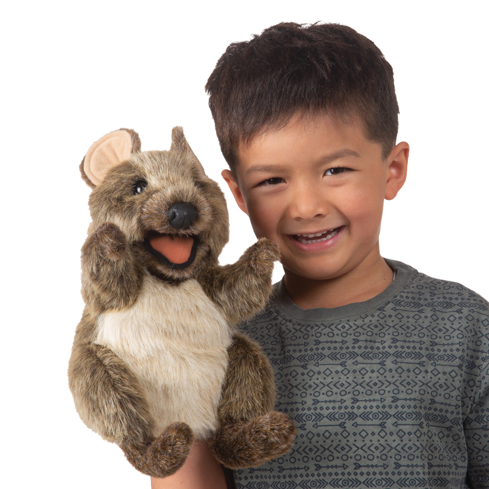 Smiling boy holds up a Folkmanis quokka hand puppet with an open mouth and brown plush fur
