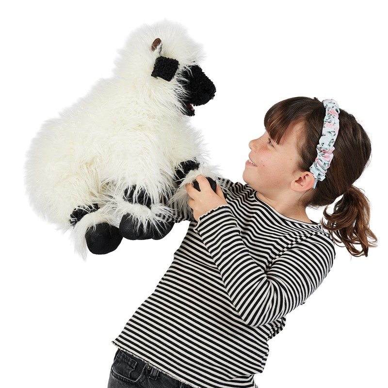 Girl holding up a Folkmanis hand puppet Valais Blacknose Sheep with white long-pile fur and black face mask