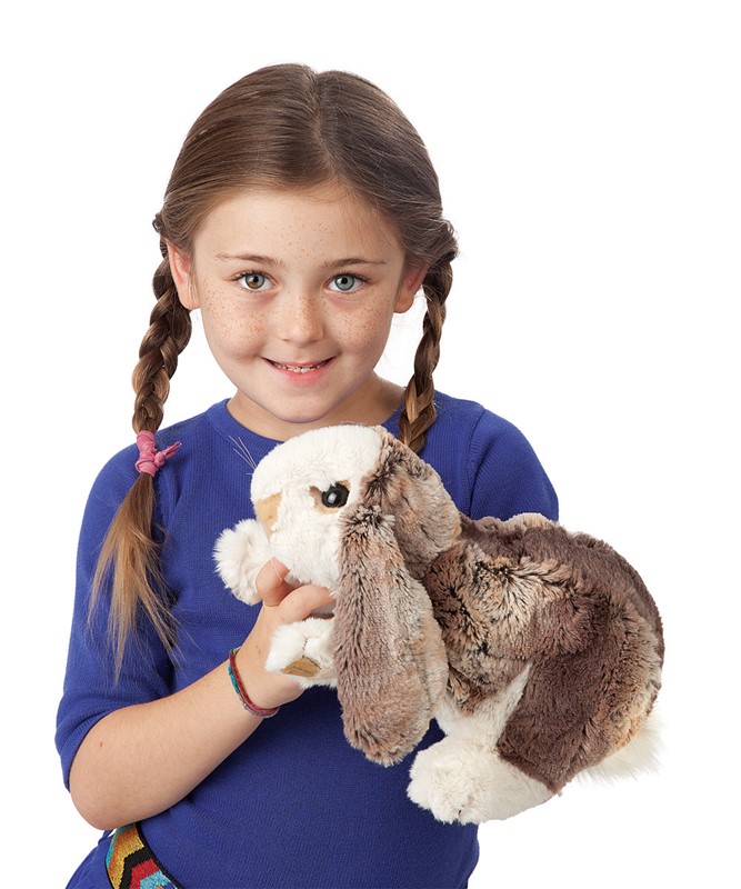 Mädchen hält Folkmanis Handpuppe Hängeohr-Hasenbaby mit braun-weißem Fell und langen Schlappohren in die Kamera.