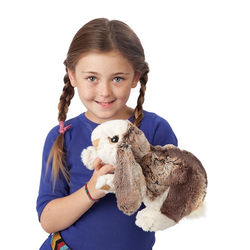 Mädchen hält Folkmanis Handpuppe Widderkaninchen-Baby mit braun-weißem Fell und langen Schlappohren in die Kamera.
