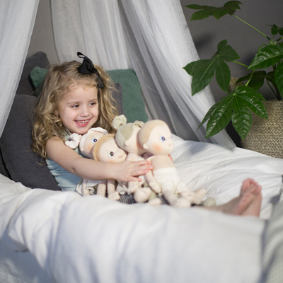 Child playing with the Rubens EcoBuds dolls on a bed with canopy
