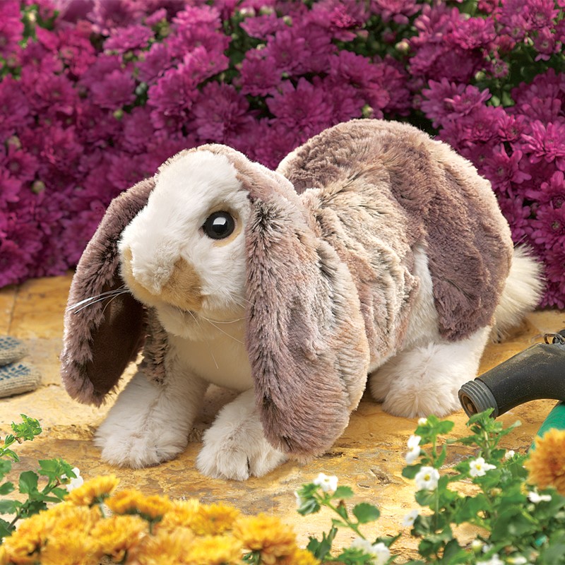 Folkmanis Handpuppe Hängeohr-Hasenbaby mit graubraunem Fell und langen herabhängenden Ohren, seitliche Ansicht vor Blumenhintergrund