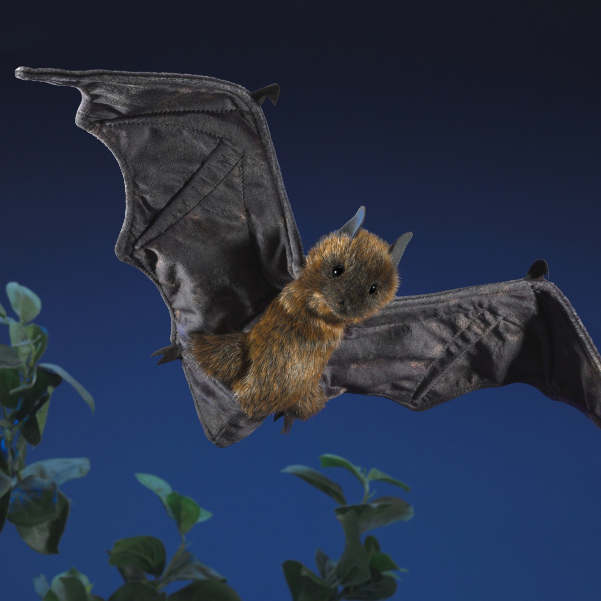 Folkmanis Handpuppe Flughund mit ausgebreiteten dunkelgrauen Flügeln und rostbraunem Fell, in Flugpose vor nachtblauem Hintergrund