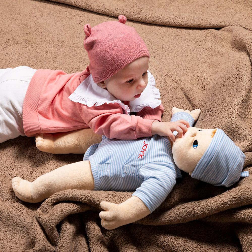 Baby looking at the same-sized Joyk empathy doll Baby Elias on a cuddly blanket