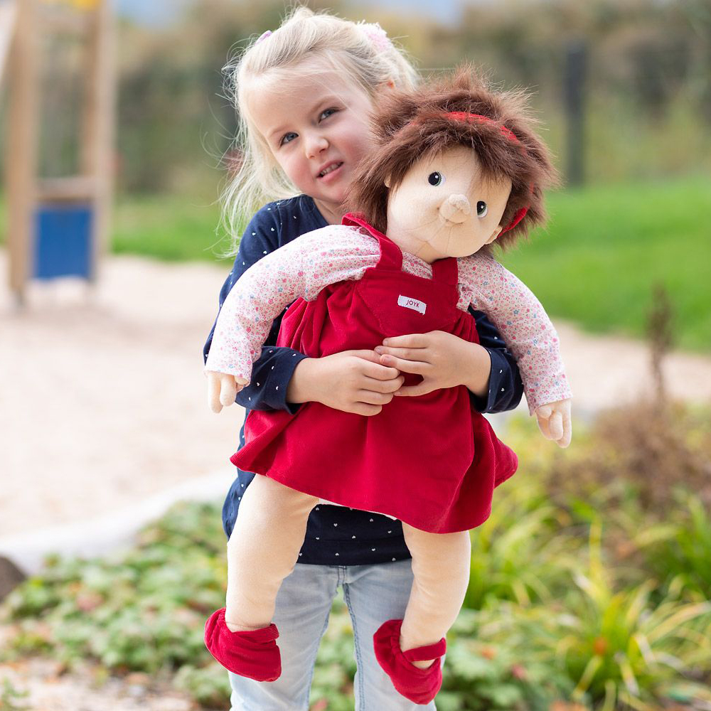 Child carrying the Joyk empathy doll Ingrid in their arms outdoors