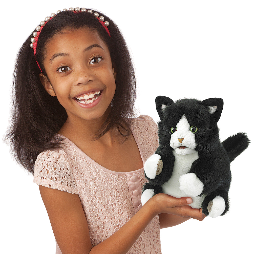 Girl holding the Folkmanis Tuxedo Kitten hand puppet with black-and-white fur and green eyes toward the camera