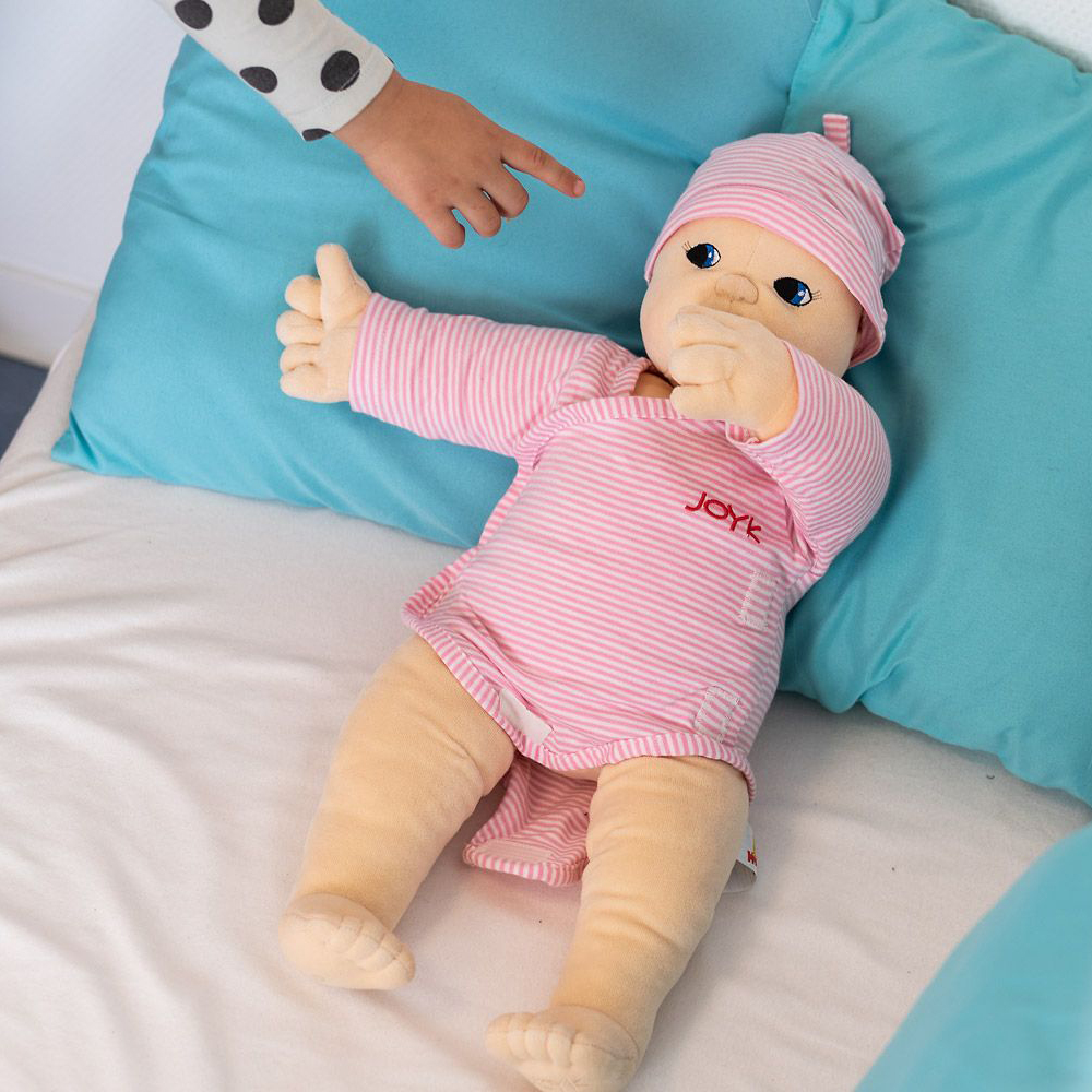 Joyk empathy doll Baby Lilly lying on a bed with turquoise cushions
