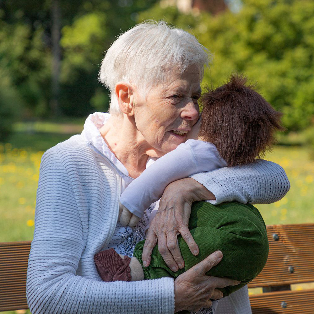 Senior lady hugging the Joyk empathy doll Marco on a park bench