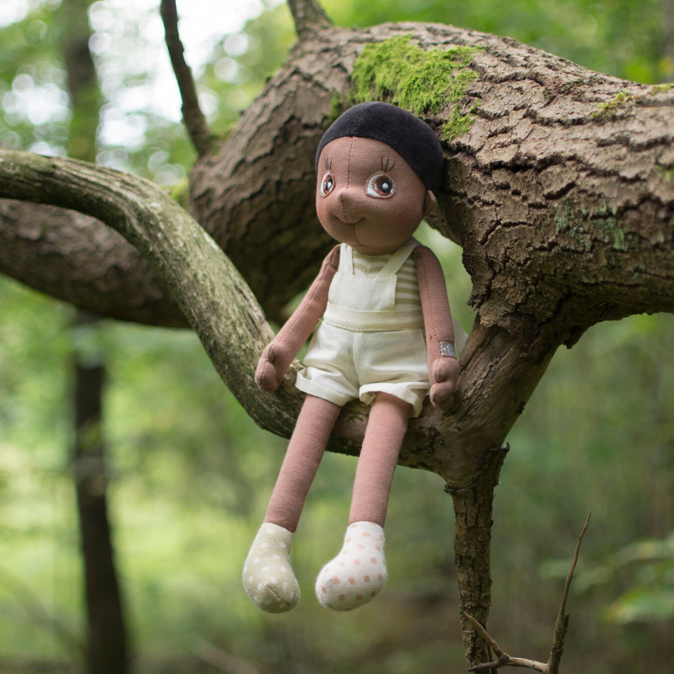 The Rubens EcoBuds doll Fern sitting on a tree branch in the green