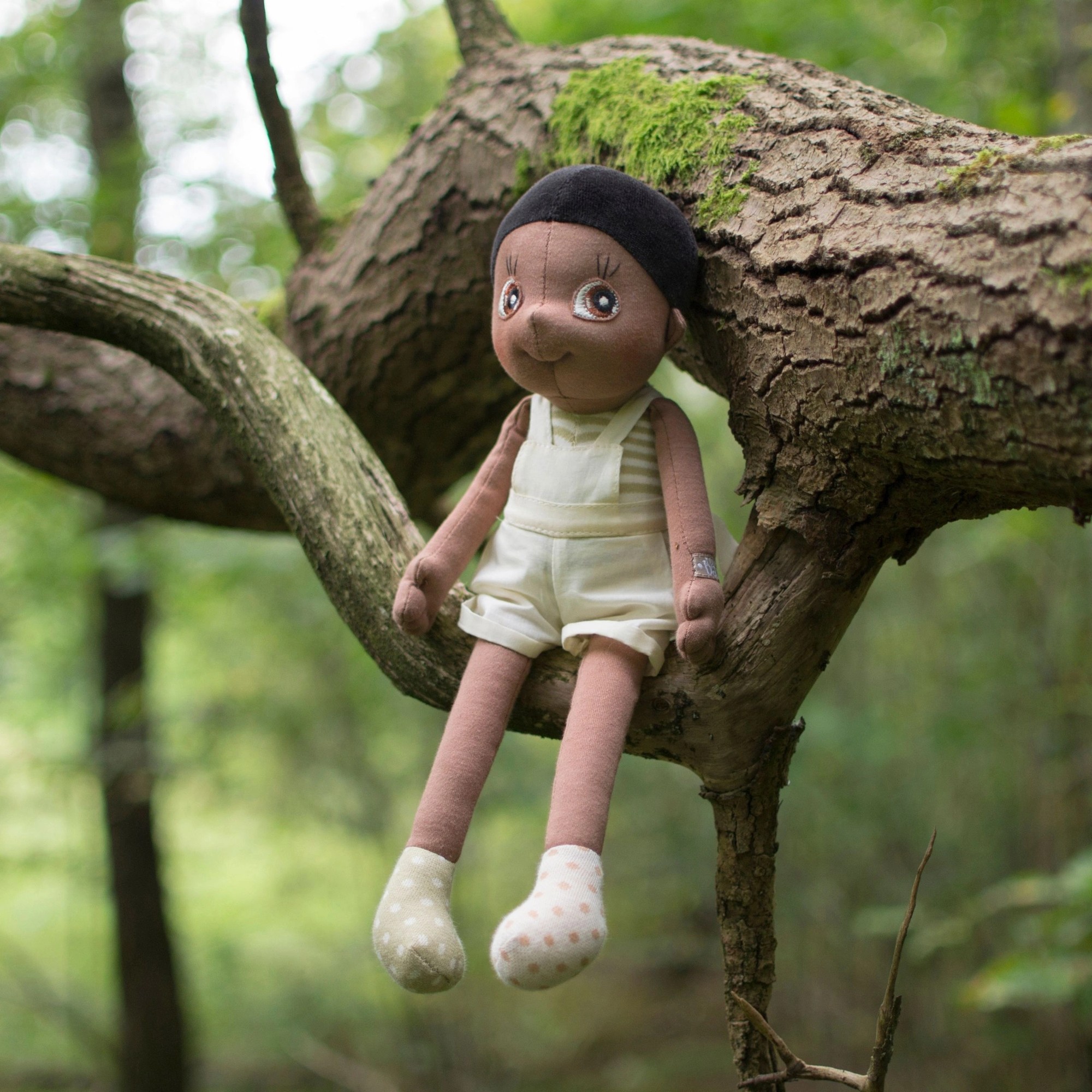 The Rubens EcoBuds doll Fern sitting on a tree branch in the green