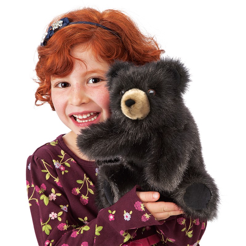 Folkmanis hand puppet baby black bear with beige muzzle area and black fur, held by a smiling girl