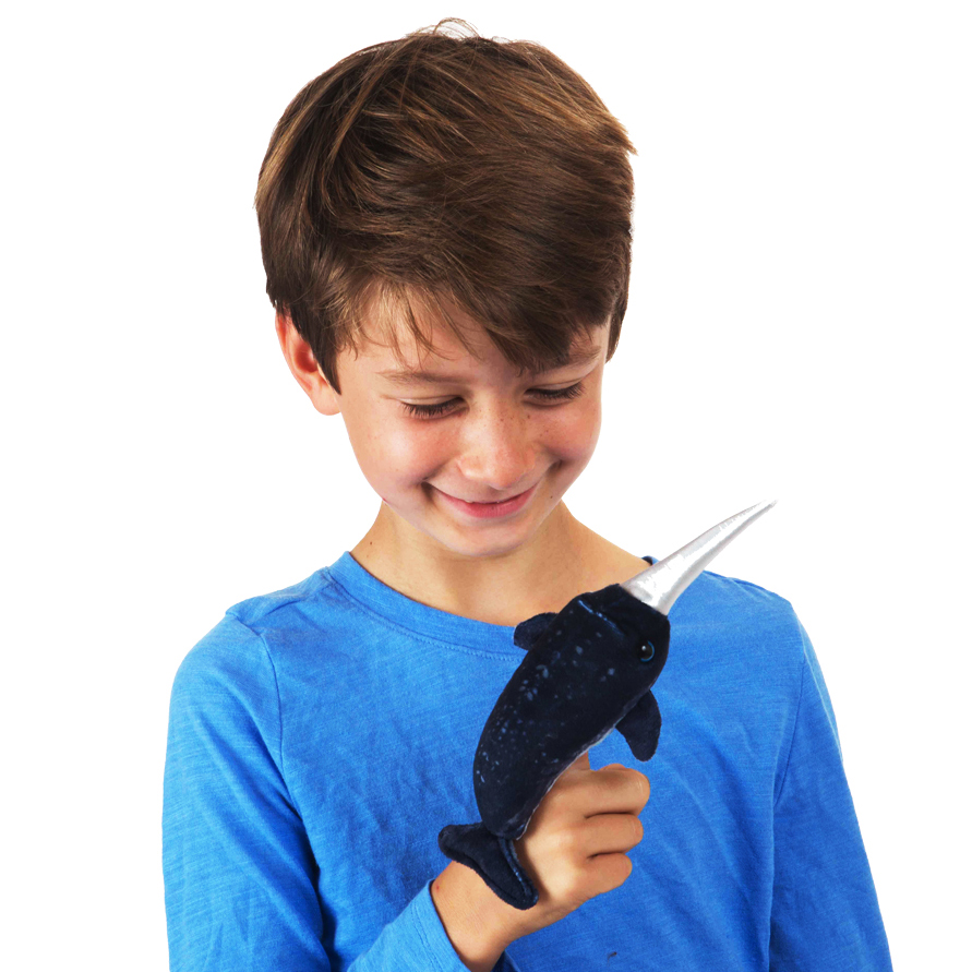 Boy in a blue jumper smiling while wearing the Folkmanis mini narwhal finger puppet in dark blue with a silver horn on his finger