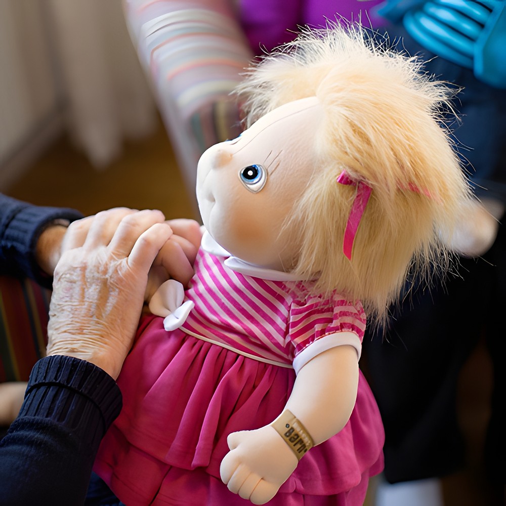 Senior lady touching the Rubens Barn Original doll Ida in a pink dress