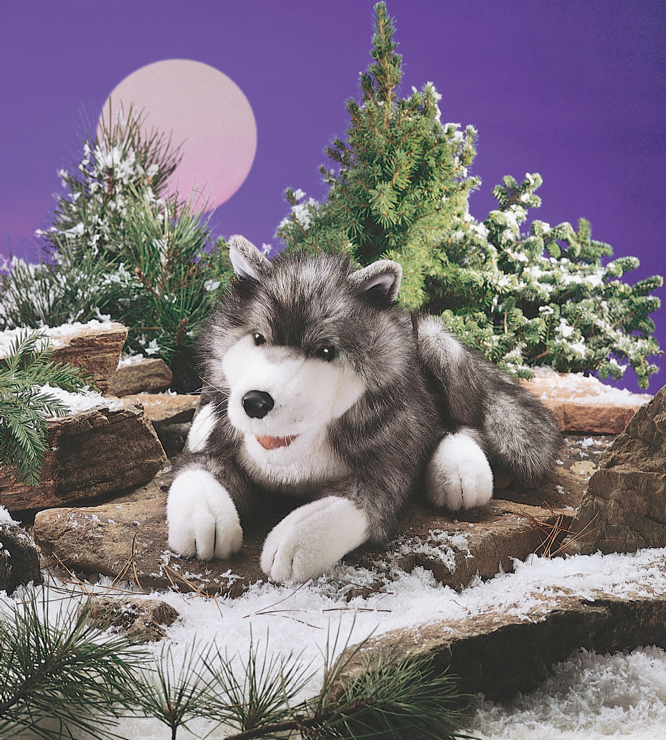 Folkmanis Handpuppe Timberwolf in Grau-Weiß, liegend auf Felsen vor verschneiter Winterkulisse mit Mondscheibe