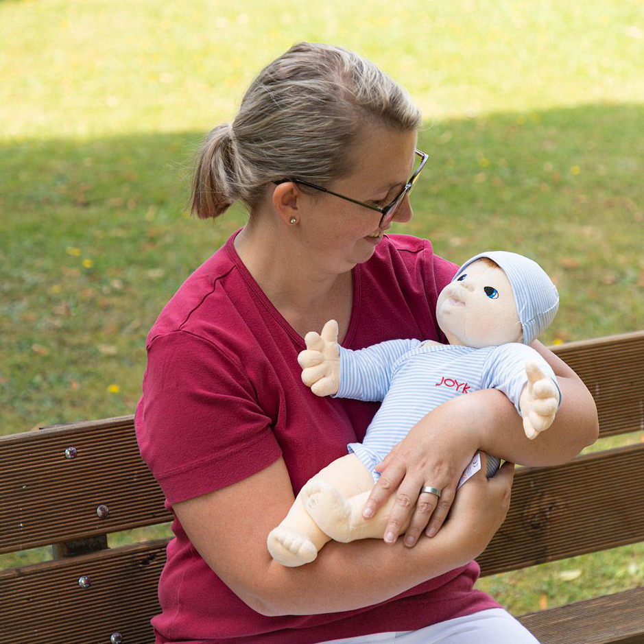 Woman holding the Joyk empathy doll Baby Elias in her arms on a park bench