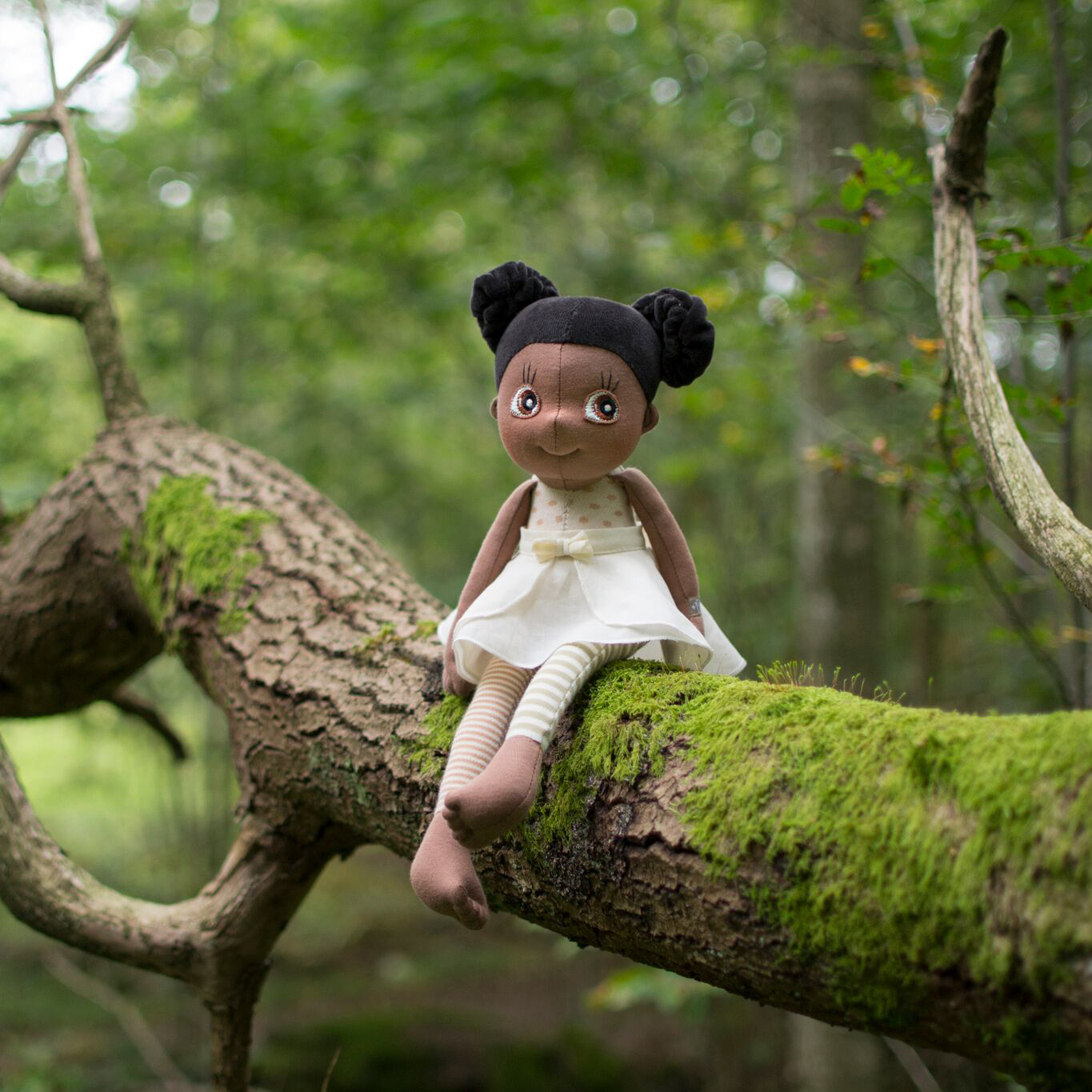 The Rubens EcoBuds doll Poppy sitting on a mossy tree trunk in the forest