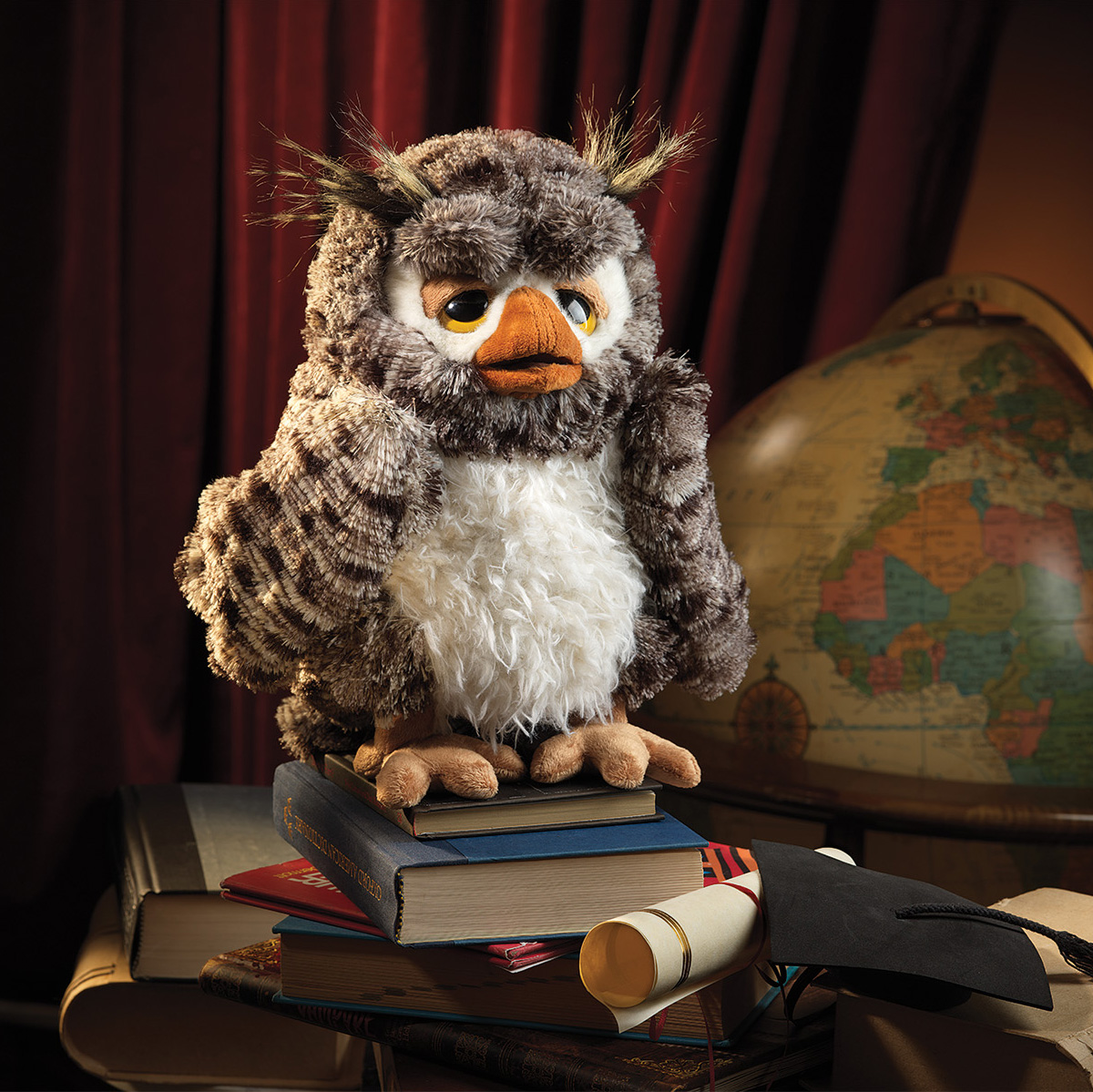 Folkmanis wise owl hand puppet with brown-grey plumage and white belly, perched on a stack of books in front of a globe