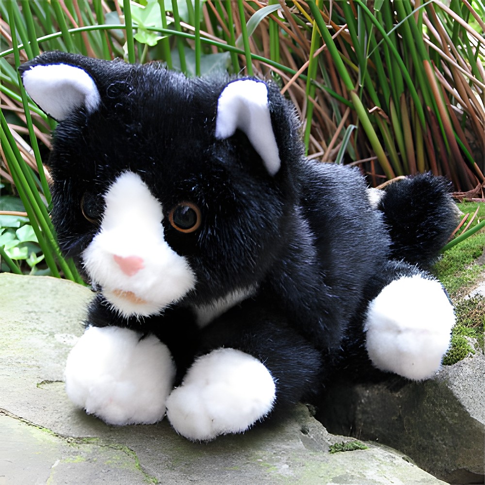 Living Puppets hand puppet black and white cat lying on a stone with grasses in the background, outdoor shot