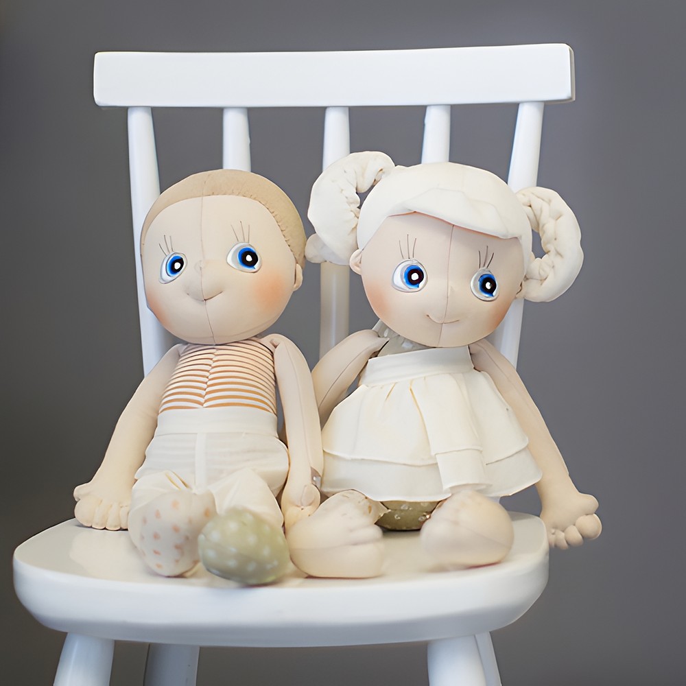 Two Rubens EcoBuds dolls on a white children's chair, Daisy on the right