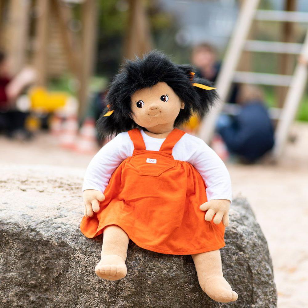 Joyk empathy doll Emelie sitting on a boulder at the edge of a playground
