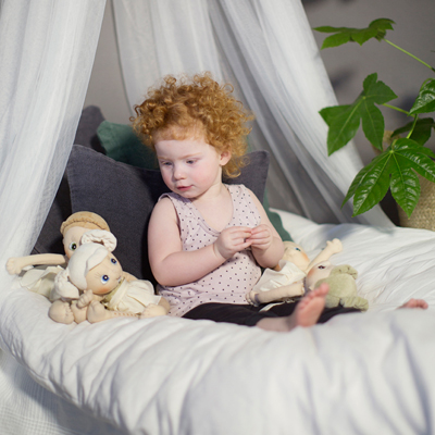 Child sitting with the Rubens EcoBuds doll Daisy under a bed canopy