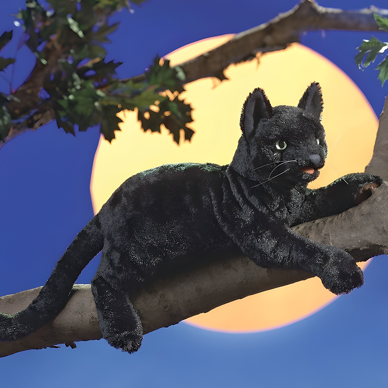 Folkmanis black cat hand puppet lying on a branch in front of a large full moon, side view