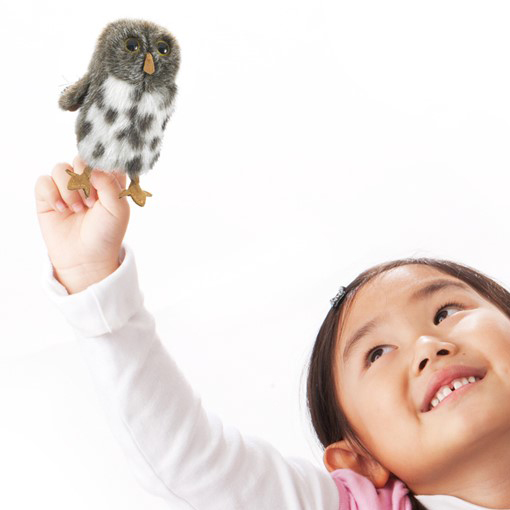 Folkmanis mini Spotted Owl finger puppet grey-and-white spotted, shown on the index finger of a smiling girl