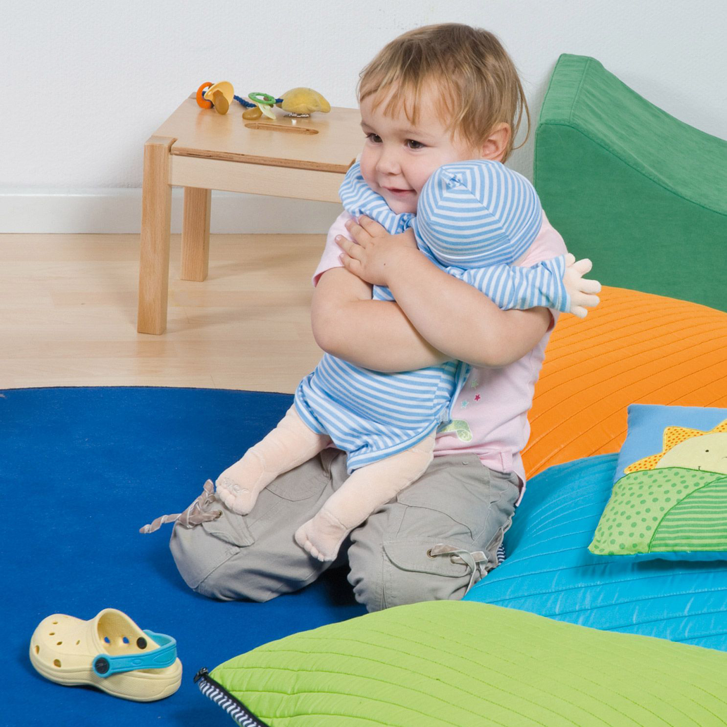 Toddler hugging the Joyk empathy doll Baby Elias on a play mat