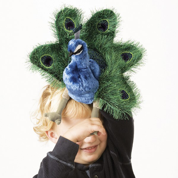 Child holding a Folkmanis small peacock hand puppet in front of their face, with blue plumage and a green fan of eye-spot feathers