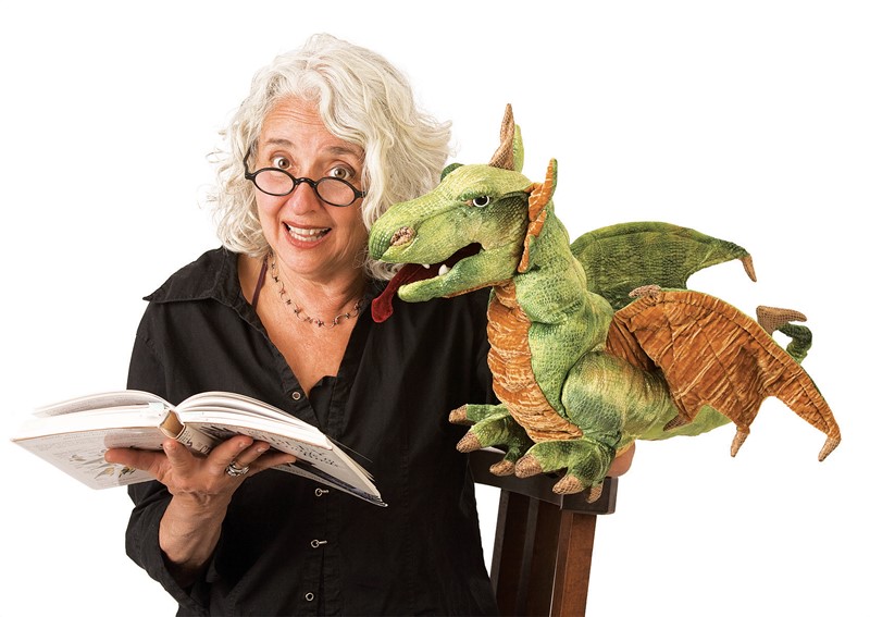 Folkmanis hand puppet wyvern dragon in green with wings, sitting on the shoulder of a woman holding a book