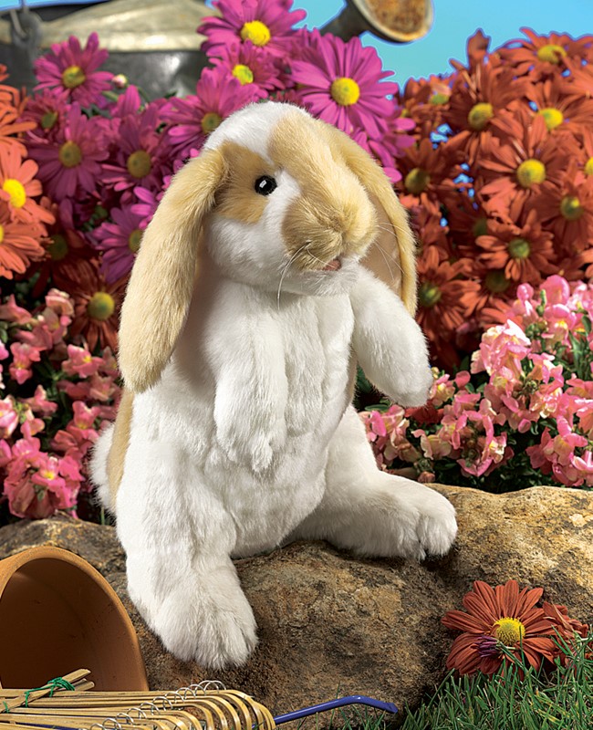 Folkmanis Handpuppe stehendes Widderkaninchen, weißes Plüschfell mit beigen Schlappohren, aufrecht auf Stein vor Blumenhintergrund
