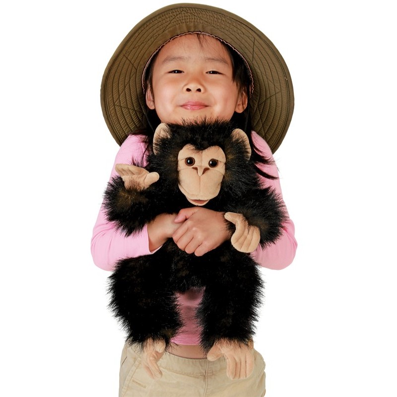 Folkmanis baby chimpanzee hand puppet with black plush fur and beige face, held by a child wearing a safari hat
