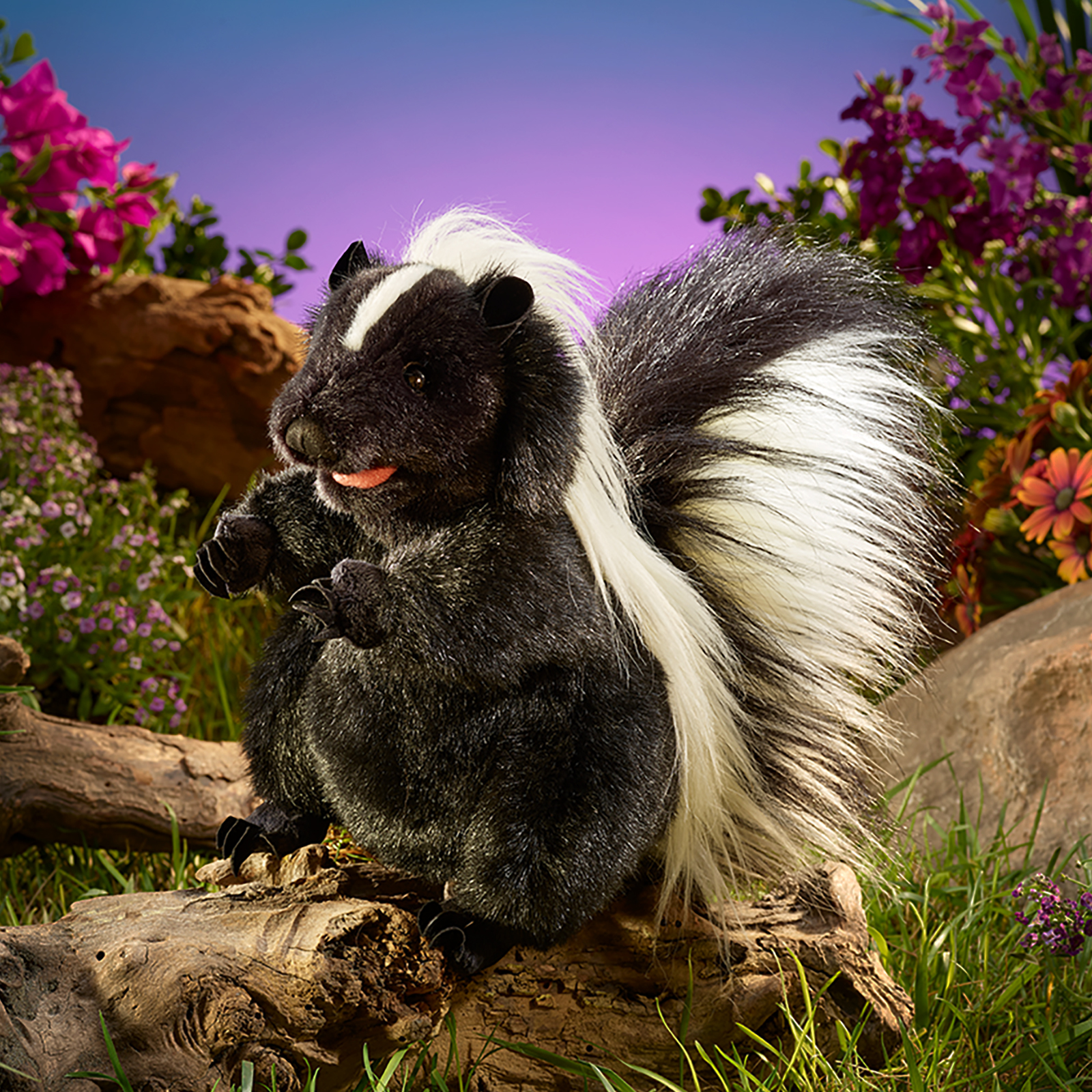 Folkmanis standing skunk hand puppet standing on a branch among flowers, its mouth open with the tongue showing.