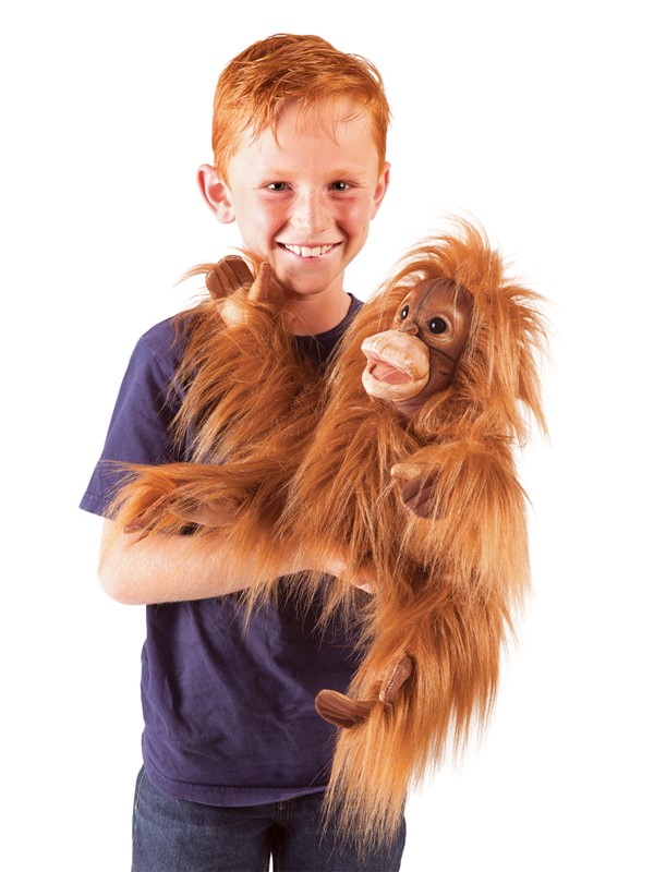 Boy holding a Folkmanis baby orangutan hand puppet with shaggy reddish-brown fur and a movable mouth against a white background