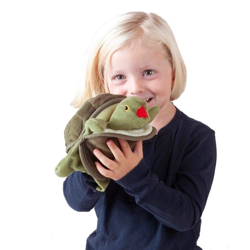 Lächelndes Kind hält die Folkmanis Handpuppe Baby Schildkröte mit grünem Kopf und rotem Maul in beiden Händen.