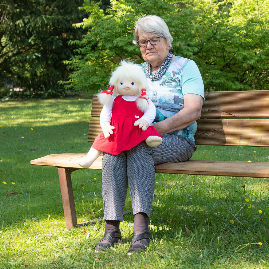 Senior lady sitting with the Joyk empathy doll Nelly on a park bench